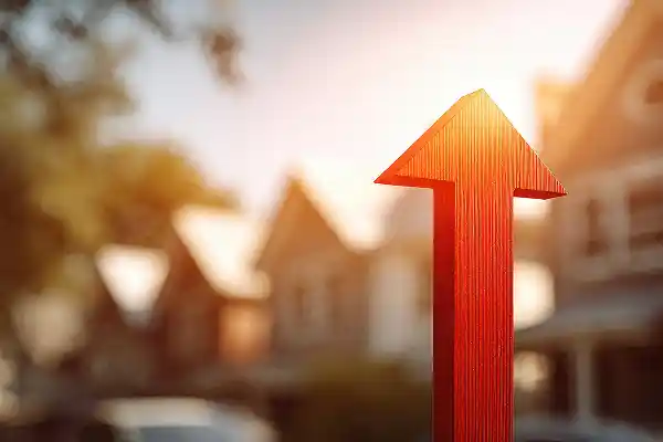 A red wooden arrow points upward with blurred houses and trees in the background. The scene is brightly lit, suggesting growth and optimism.