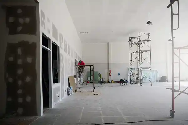 Spacious, unfinished interior with scaffolding, partially painted walls, and construction materials scattered. Quiet, in-progress work setting.