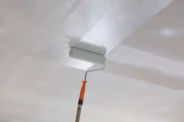 A paint roller applies a fresh coat of white paint to a ceiling, creating a smooth, clean surface. The scene conveys a sense of renovation and freshness.